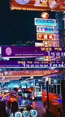 A vibrantly lit up street at night in Bangkok with signs in Thai and colorful lights.