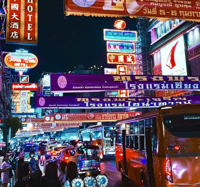 A vibrantly lit up street at night in Bangkok with signs in Thai and colorful lights.