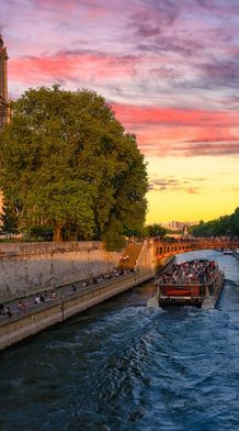 Notre-Dame Cathedral by the Seine River at sunset, with a boat full of people and a colorful sky.