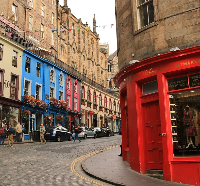 A vibrant street scene with colorful buildings, people walking, and a red shop on a cobblestone road under a decorated string of flags.