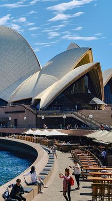 Sydney Opera House with its iconic sails, waterfront promenade, outdoor seating, and people enjoying a sunny day.