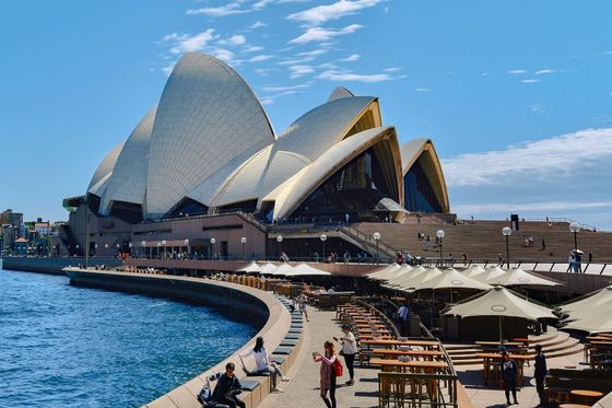 Sydney Opera House with its iconic sails, waterfront promenade, outdoor seating, and people enjoying a sunny day.