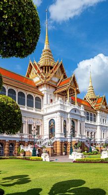 A grand palace with ornate, golden spires and white facades, surrounded by lush, manicured gardens under a bright blue sky with fluffy clouds.