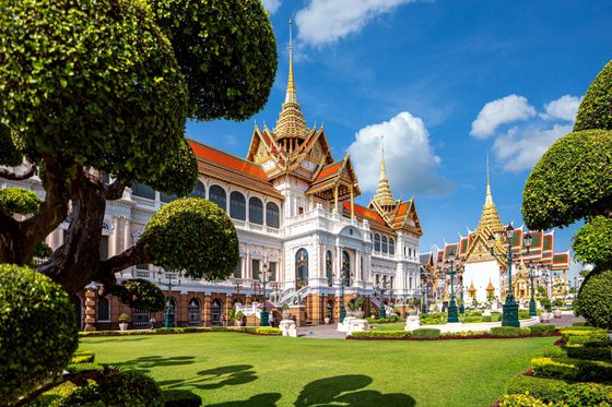 A grand palace with ornate, golden spires and white facades, surrounded by lush, manicured gardens under a bright blue sky with fluffy clouds.