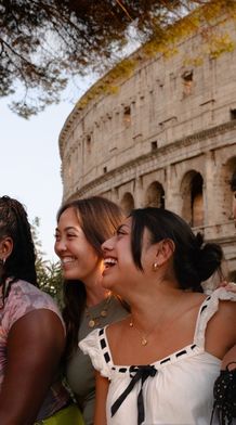 Five people smiling near the Colosseum at sunset, with trees and the ancient structure in the background.