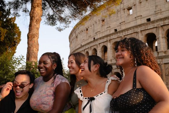 Five people smiling near the Colosseum at sunset, with trees and the ancient structure in the background.