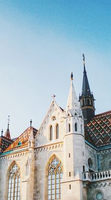 Gothic-style cathedral with ornate spire, colorful tiled roof, and arched windows under a clear blue sky.