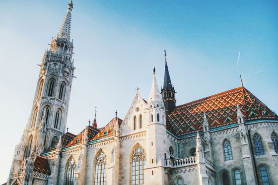 Gothic-style cathedral with ornate spire, colorful tiled roof, and arched windows under a clear blue sky.