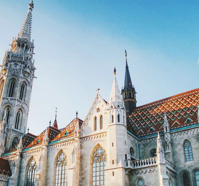 Gothic-style cathedral with ornate spire, colorful tiled roof, and arched windows under a clear blue sky.