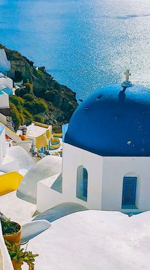 Santorini's white buildings with blue domes overlook the shimmering Aegean Sea under a clear sky.