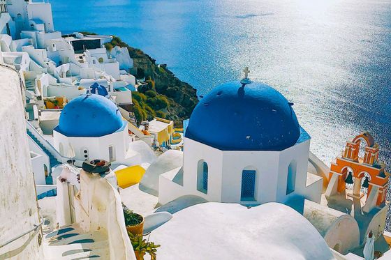 Santorini's white buildings with blue domes overlook the shimmering Aegean Sea under a clear sky.