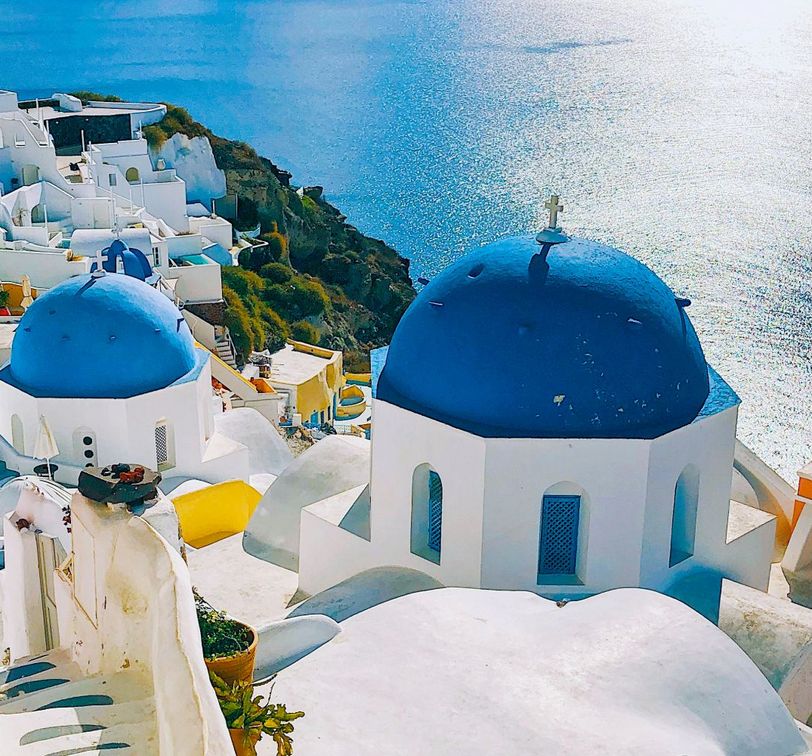 Santorini's white buildings with blue domes overlook the shimmering Aegean Sea under a clear sky.