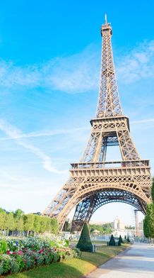 The Eiffel Tower surrounded by green trees and colorful flowers under a clear blue sky.