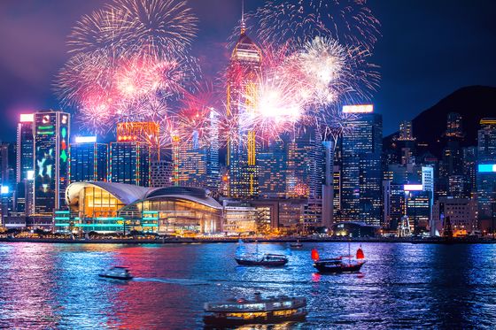 Vibrant fireworks illuminate a city skyline at night, with boats on the water reflecting colorful lights from the display and surrounding buildings.