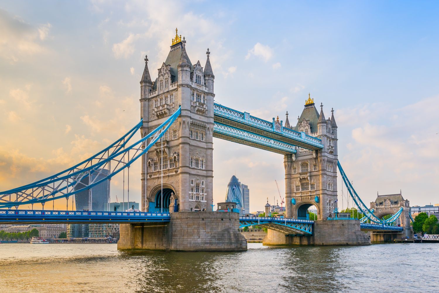 Tower Bridge in London at sunset, with its iconic twin towers and blue suspension accents, spanning the River Thames.