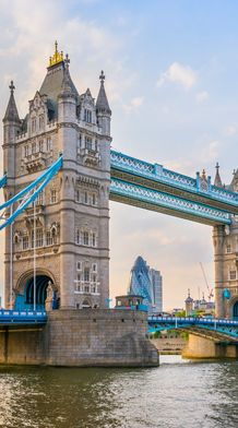 Tower Bridge in London at sunset, with its iconic twin towers and blue suspension accents, spanning the River Thames.