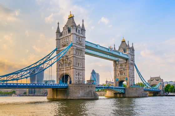 Tower Bridge in London at sunset, with its iconic twin towers and blue suspension accents, spanning the River Thames.