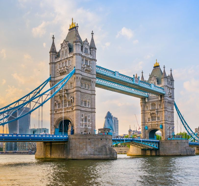 Tower Bridge in London at sunset, with its iconic twin towers and blue suspension accents, spanning the River Thames.