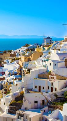 Whitewashed buildings with blue domes on a cliffside overlooking the sea in Santorini, Greece, with a clear blue sky above.