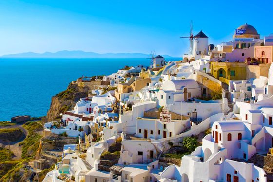 Whitewashed buildings with blue domes on a cliffside overlooking the sea in Santorini, Greece, with a clear blue sky above.