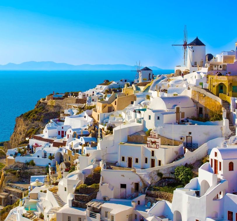 Whitewashed buildings with blue domes on a cliffside overlooking the sea in Santorini, Greece, with a clear blue sky above.