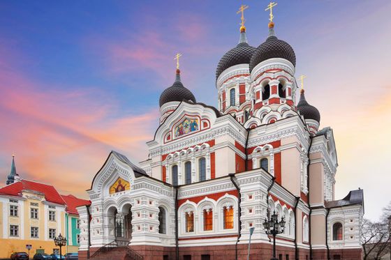 Ornate building with onion domes and crosses, featuring intricate white and red detailing, set against a colorful sunset sky.