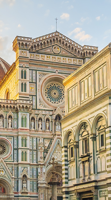 The Florence Cathedral, with its intricate facade and large dome, is bathed in warm sunlight against a clear sky.