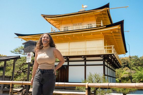Woman smiling in front of a golden temple with a bright blue sky above.