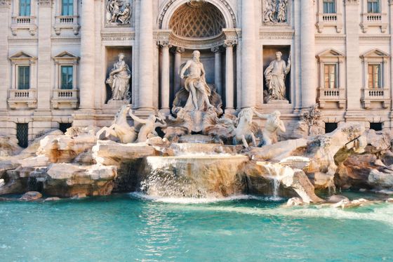 The Trevi Fountain in Rome, featuring elaborate sculptures of Oceanus, horses, and Tritons, with water cascading into a turquoise pool.