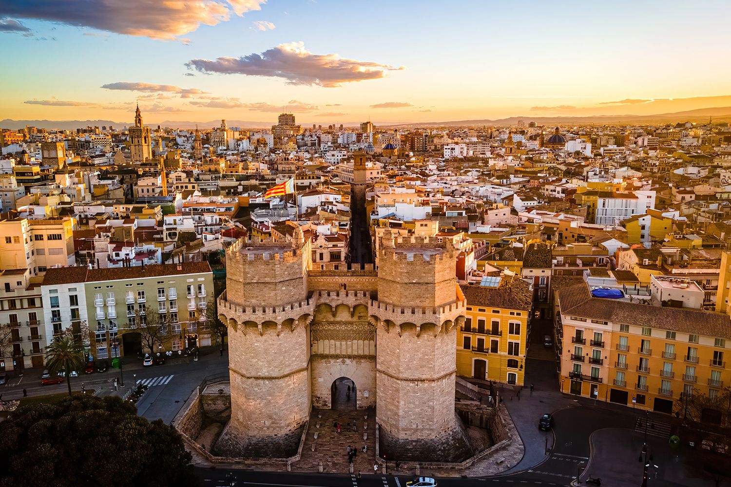 Aerial view of Valencia's Torres de Serranos at sunset, surrounded by city buildings under a sky with scattered clouds.