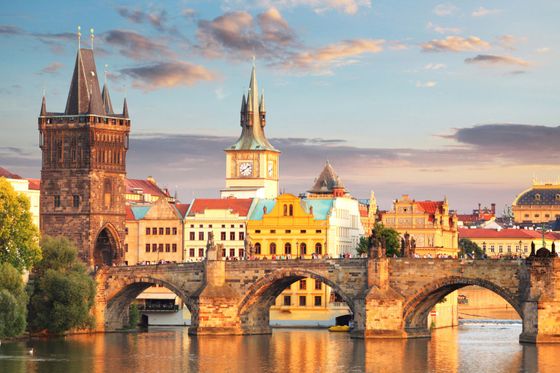 Historic stone bridge over a river with arched piers, surrounded by colorful buildings and a clock tower under a partly cloudy sky.
