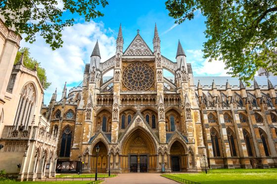 Gothic-style cathedral with intricate spires, large rose window, and arched entrances, surrounded by greenery under a clear blue sky.