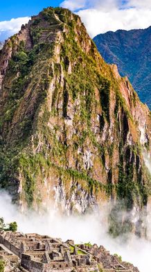 Ancient stone ruins of Machu Picchu surrounded by lush mountains and mist under a blue sky.