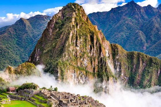 Ancient stone ruins of Machu Picchu surrounded by lush mountains and mist under a blue sky.