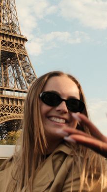 Two women smiling and wearing sunglasses with the Eiffel Tower in the background under a blue sky.