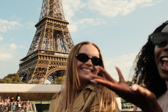 Two women smiling and wearing sunglasses with the Eiffel Tower in the background under a blue sky.