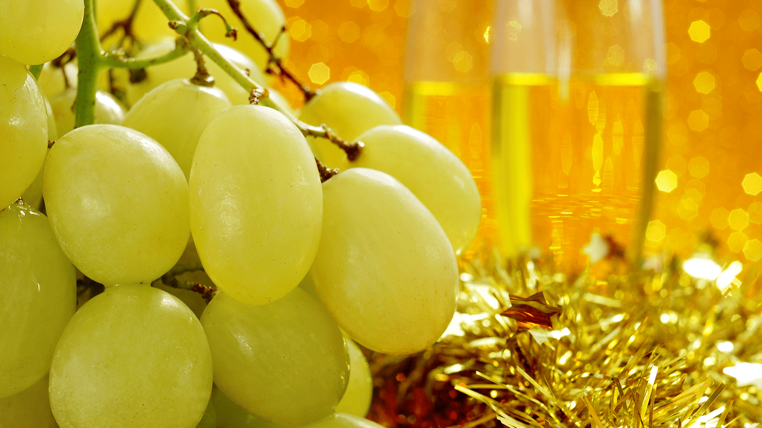 A festive closeup of green grapes, gold tinsel, and flutes of champagne.