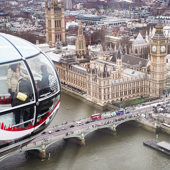 Aerial view of the London Eye capsule with people inside, overlooking Westminster Palace, Big Ben, and the River Thames from above.