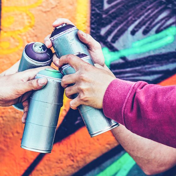 Four hands holding spray paint cans in a group gesture, with a colorful graffiti wall in the background.
