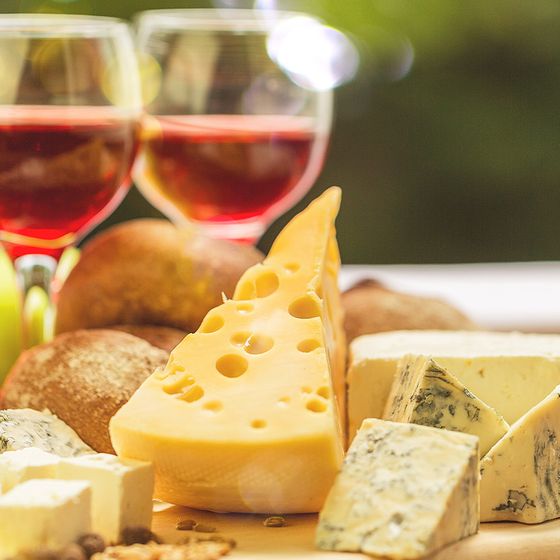 A cheese platter with various cheeses, bread, and two glasses of red wine in a warm, softly lit setting.