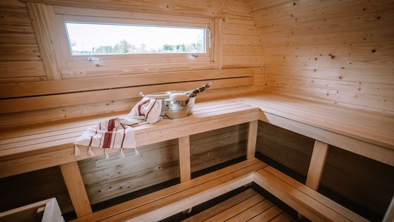 Wooden sauna interior with benches, a metal bucket, a towel, and a small window.