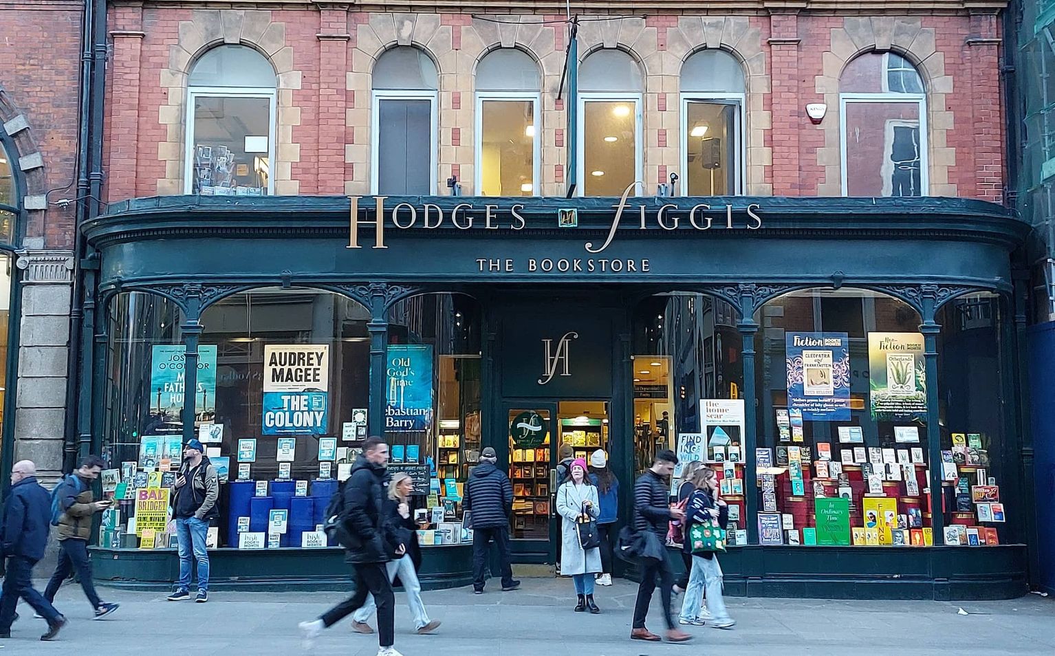 Street view of Hodges Figgis bookstore with pedestrians passing by, showcasing a large window display of various books.