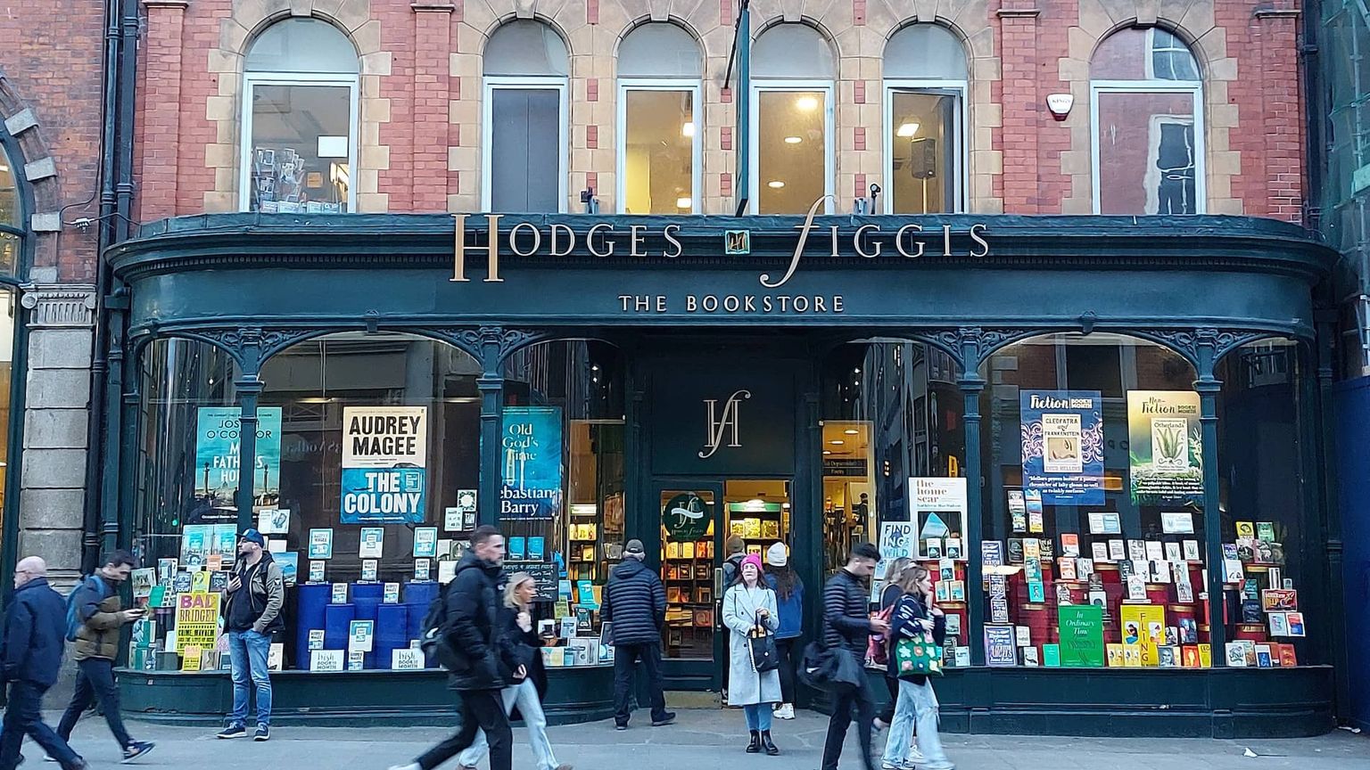 Street view of Hodges Figgis bookstore with pedestrians passing by, showcasing a large window display of various books.