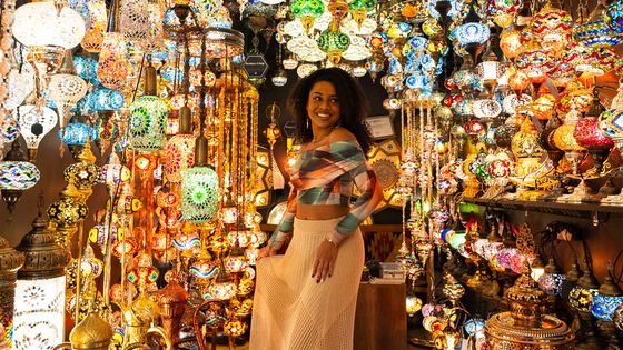 Woman standing among a vibrant display of colorful, intricately designed lamps in a shop filled with warm, glowing lights.