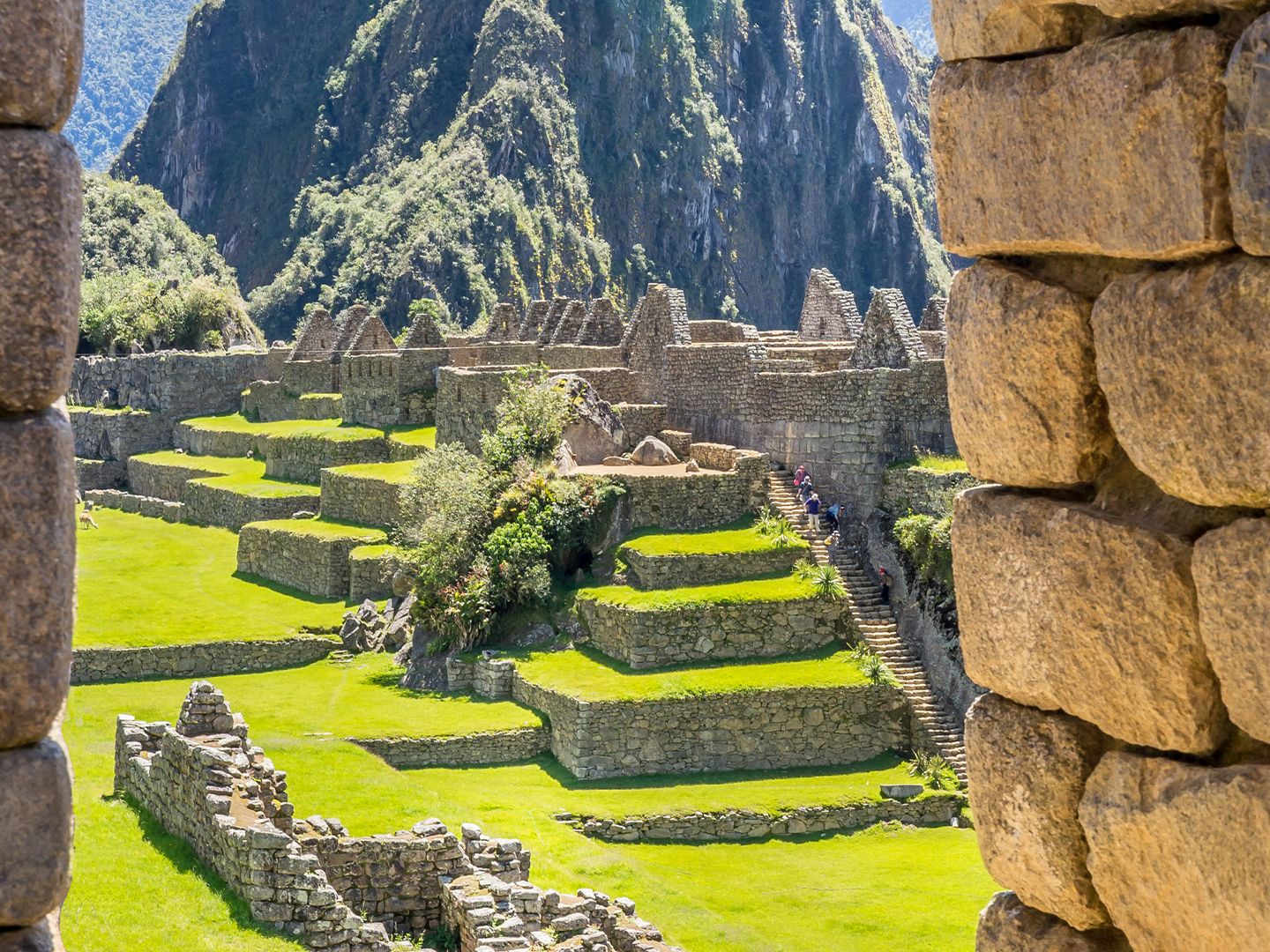 View of Machu Picchu ruins framed by stone walls, featuring terraces and mountains under a clear blue sky.