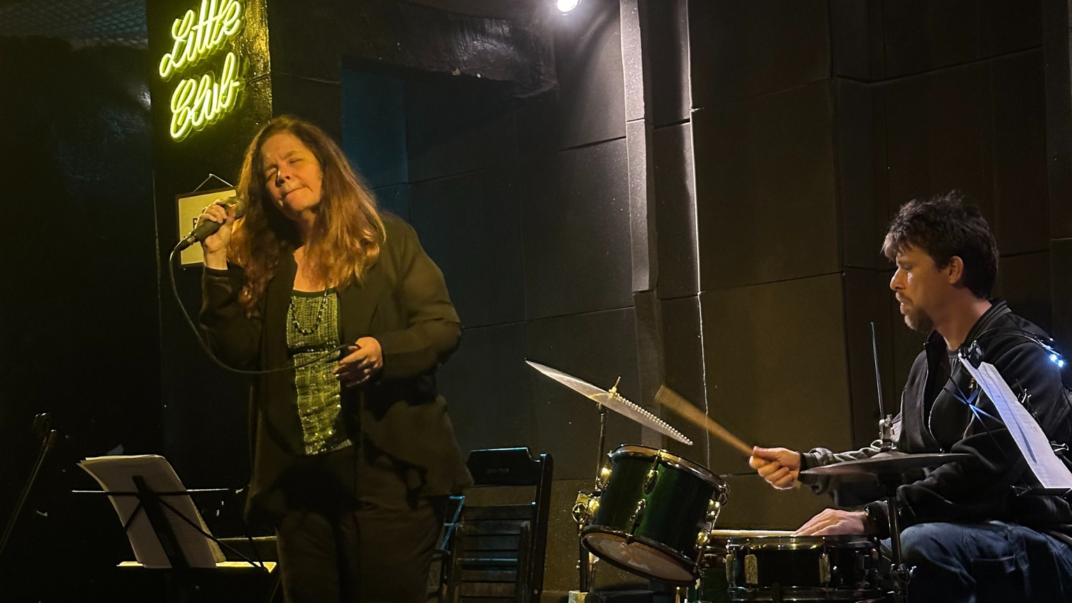 A woman singing Bossa Nova next to a man playing the drums.