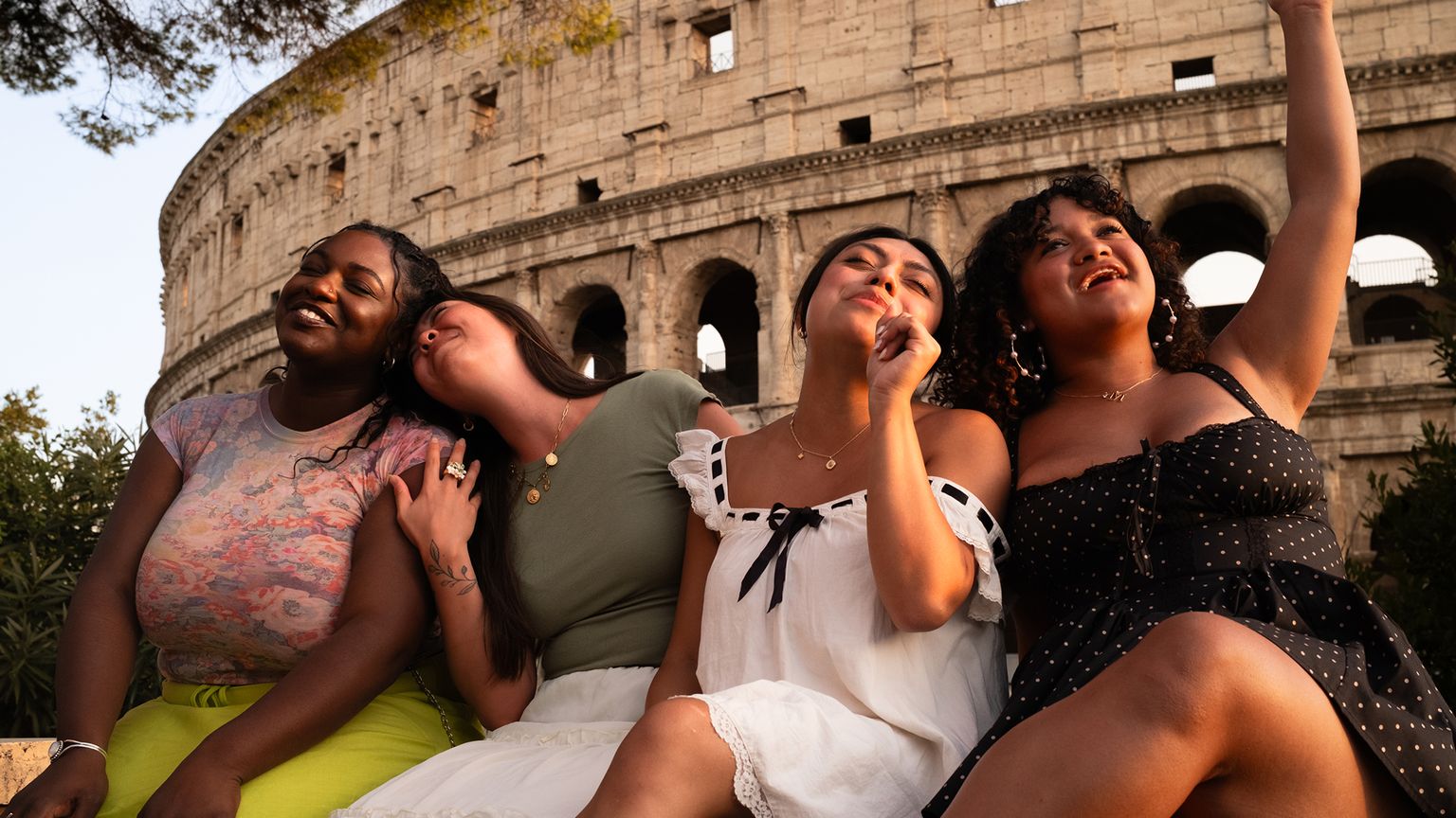 Four women sitting and smiling in front of the Colosseum in Rome, enjoying the sunset and each other's company.