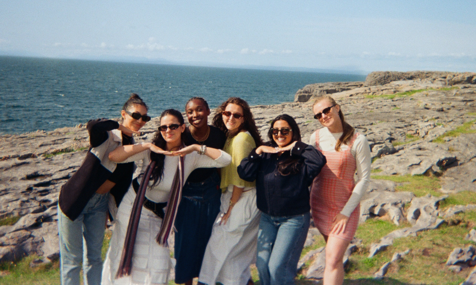 A group of people posing on a cliff with the water in the distance.