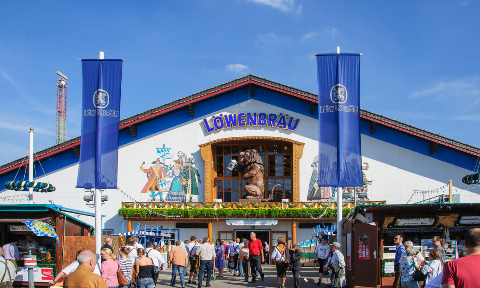 Outside of the Löwenbräu-Festzelt Oktoberfest tent with people walking around and the iconic lion statue above the entrance.