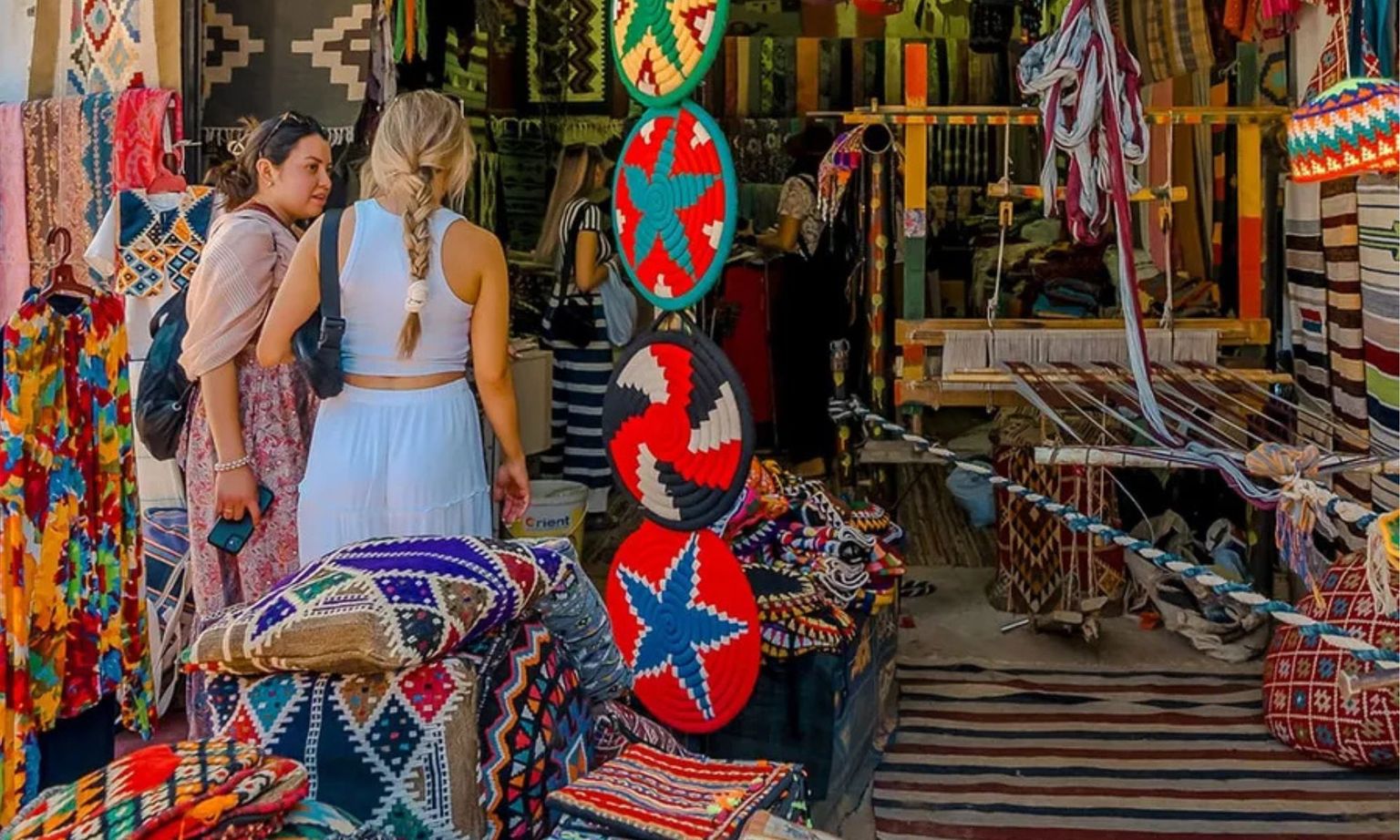 Two women talking in an Egyptian market filled with colorful textiles and handmade goods